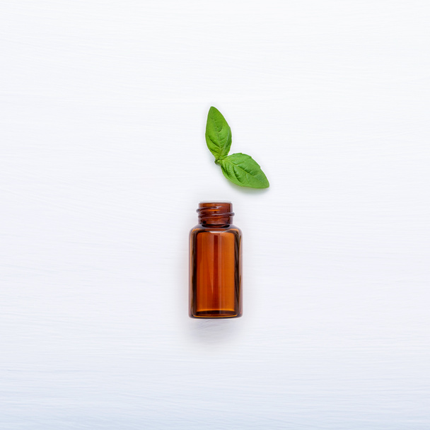 Bottle of essential oil with fresh basil leaves setup with flat lay on white wooden table. - Photo, Image