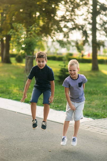 Twee kinderen spelen in het park. Twee mooie jongens in T-shirts en shorts hebben leuke glimlachen. Ze eten ijs, springen, lopen. Het is een zonnige zomer - Foto, afbeelding