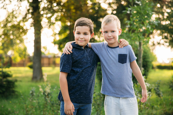 Δύο παιδιά παίζουν στο πάρκο. Δύο όμορφα αγόρια σε μπλουζάκια και Σορτσάκια να διασκεδάσουν χαμογελώντας. Τρώνε παγωτό, άλμα, τρέχει. Το καλοκαίρι είναι ηλιόλουστος - Φωτογραφία, εικόνα