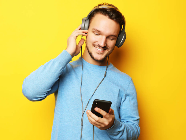 lifestyle and people concept: Happy young man listening to music with headphones over yellow background - Fotoğraf, Görsel