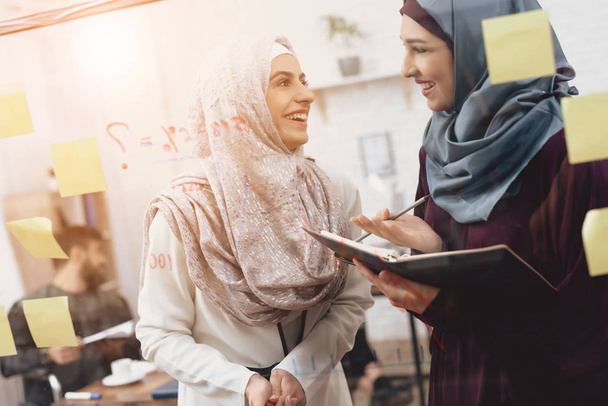 Ofiste çalışan hijab iki Arap kadınları. İş arkadaşlarınızla cam tahta üzerinde notlar alıyor. - Fotoğraf, Görsel