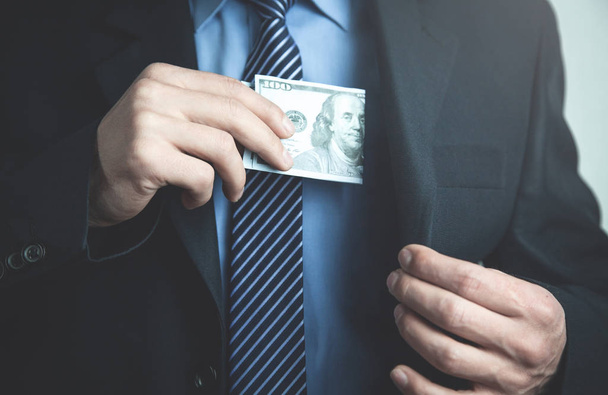 Businessman putting hundred dollar in his suit pocket. - Фото, изображение