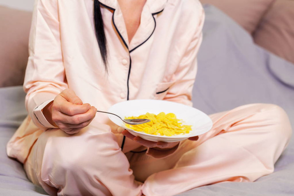Donna in pigiama mangiare cornflakes con latte nel letto
 - Foto, immagini