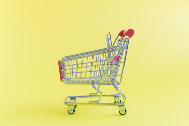 Closeup of tiny shopping cart on yellow background - 写真・画像