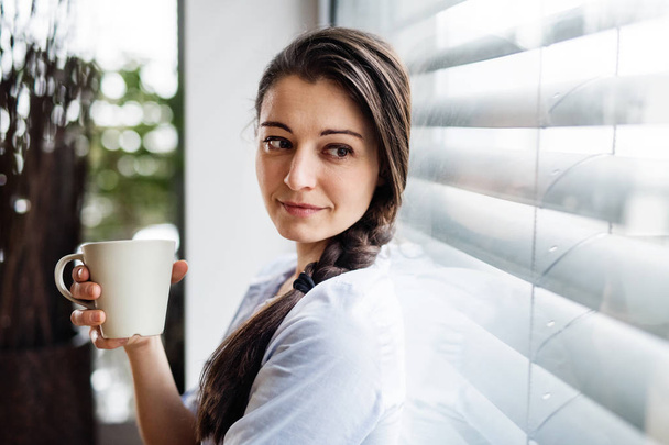 Woman by the window holding cup of coffee. - Fotoğraf, Görsel