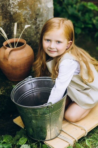 beautiful little girl with a jug and a bucket near the well  - Valokuva, kuva