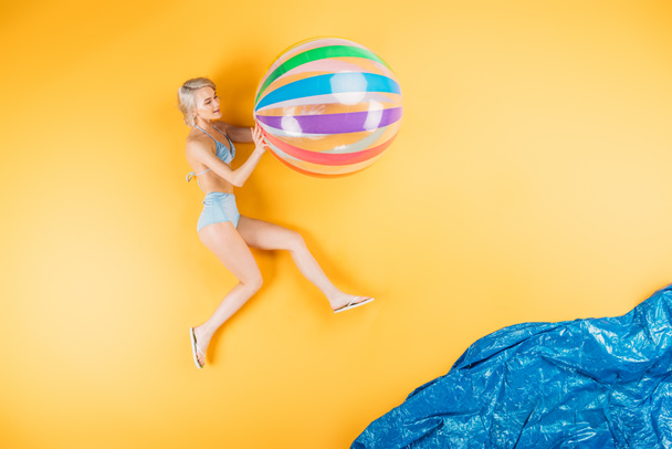 όμορφη νεαρή γυναίκα με μαγιό και σαγιονάρες εκμετάλλευση φουσκωτή μπάλα φανταστείτε παραλία - Φωτογραφία, εικόνα