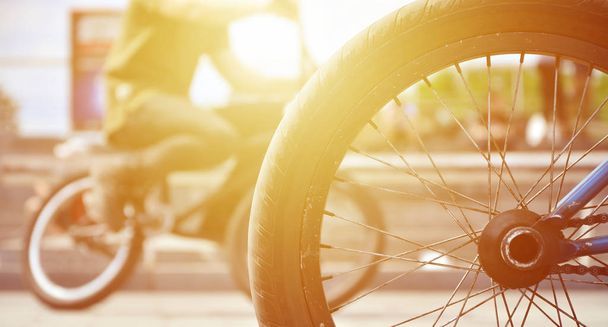 Una rueda de bicicleta BMX contra el telón de fondo de una calle borrosa con ciclistas. Concepto de deportes extremos
 - Foto, imagen