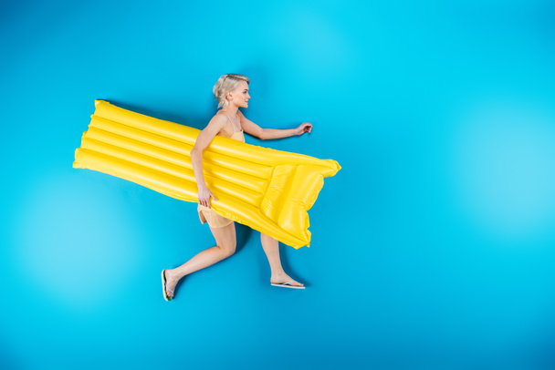 top view of beautiful girl in flip flops holding inflatable mattress on blue - Photo, Image