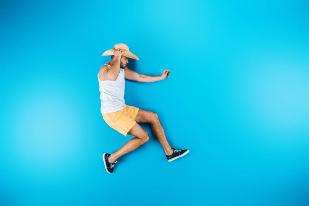 top view of young man in shorts and hat posing on blue - Foto, imagen