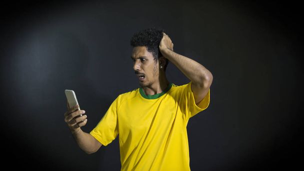 Male athlete or fan in yellow uniform looking cell phone on black background - Zdjęcie, obraz