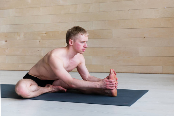 Sporty man doing Paschimottasana pose on yoga class - Фото, изображение