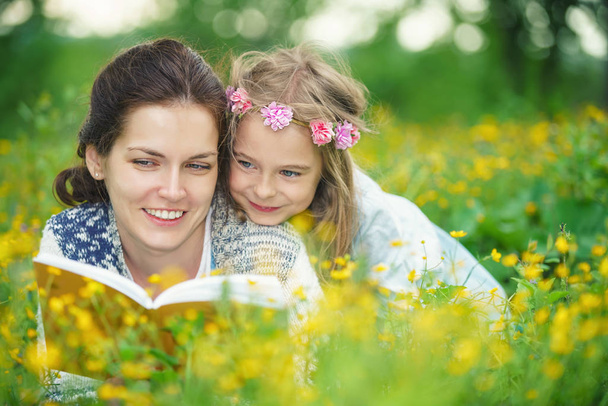 Mother and daughter reading book on green spring meadow - Fotó, kép