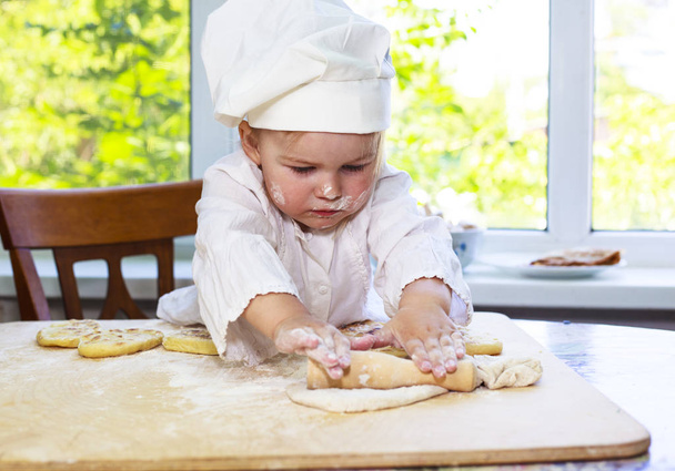 Маленькая девочка делает тест, в шапке повара, напротив окна, на кухне
. - Фото, изображение