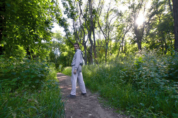 Un jeune homme en costume de sport gris se tient en face du soleil parmi les arbres de la forêt. Loisirs lors d'une course sportive en pleine forêt. L'enlèvement d'une belle aube
 - Photo, image