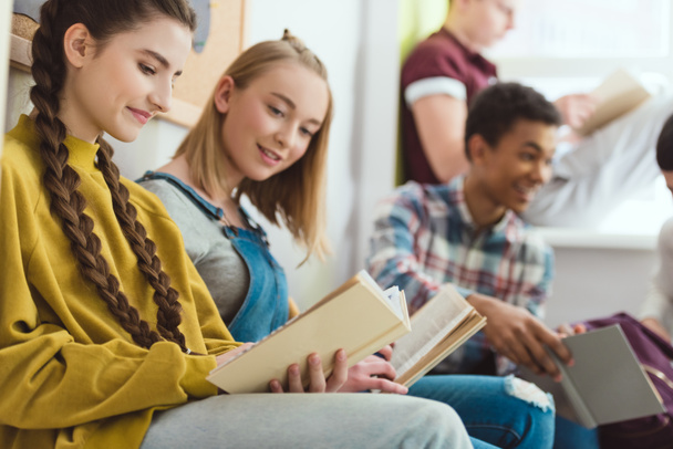 Group of smiling multicultural teenage schoolchildren reading books during school break - Photo, Image