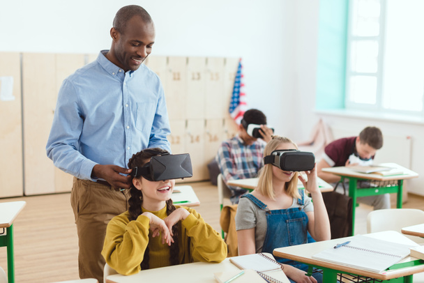 Profesor de pie y estudiantes adolescentes de secundaria multicultural usando auriculares de realidad virtual
  - Foto, Imagen