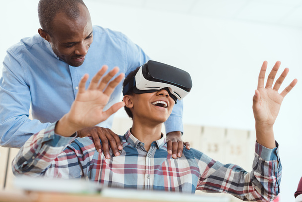 Lachende middelbare school tiener student met behulp van virtual reality headset en leraar zijn schouders te houden - Foto, afbeelding