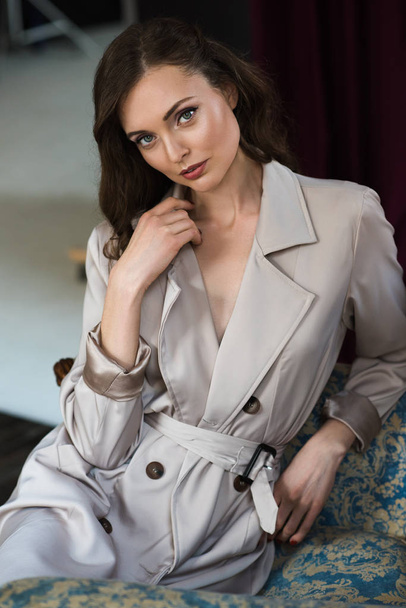 attractive woman in trench coat sitting in armchair - Zdjęcie, obraz