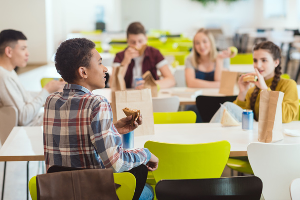 学校の食堂で昼食を取っている間チャット高校生のグループ - 写真・画像