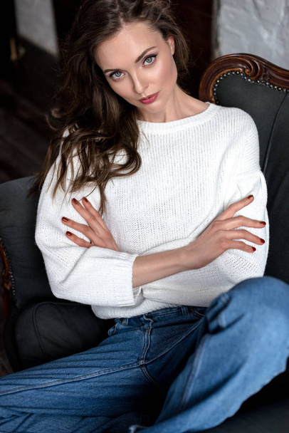 beautiful casual brunette girl with crossed arms sitting on armchair and looking at camera - Φωτογραφία, εικόνα