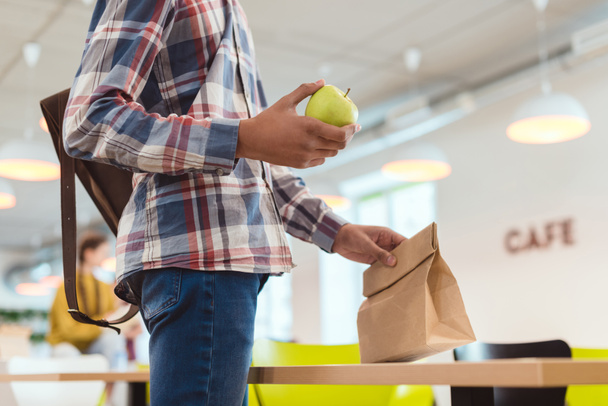 tiro recortado do estudante americano africano com maçã e saco de almoço na cafetaria da escola
 - Foto, Imagem