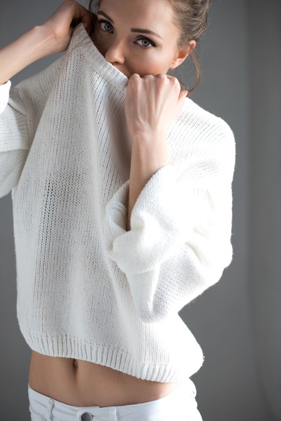 sensual young woman taking off white sweater and looking at camera on grey   - Fotó, kép