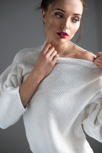 beautiful brunette woman wearing white sweater and looking away on grey - Foto, afbeelding