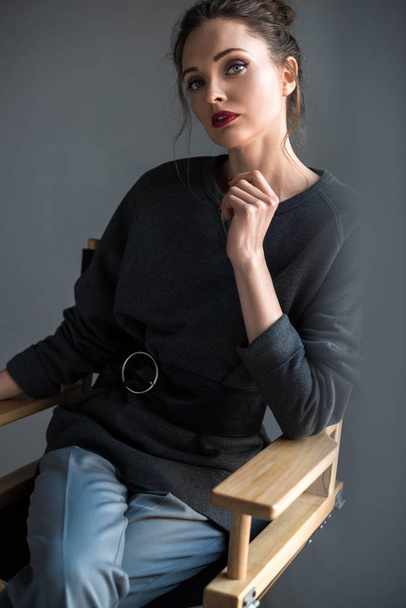 portrait of beautiful tender woman sitting on chair and looking at camera on grey - Fotoğraf, Görsel