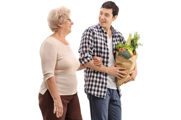Young man helping an elderly woman with her groceries isolated on white background - Zdjęcie, obraz