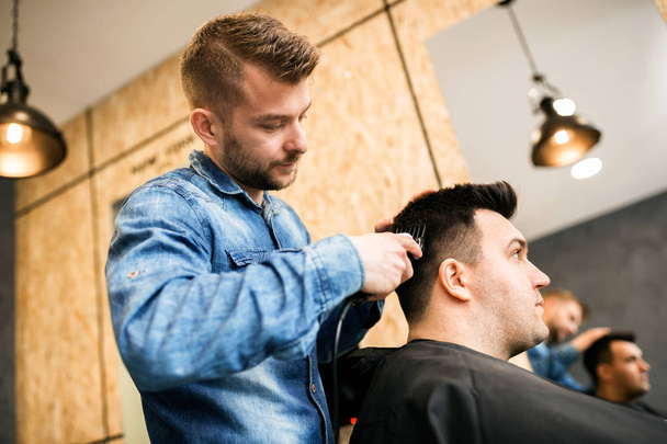 Young professional barber making haircut to customer at barber shop - 写真・画像