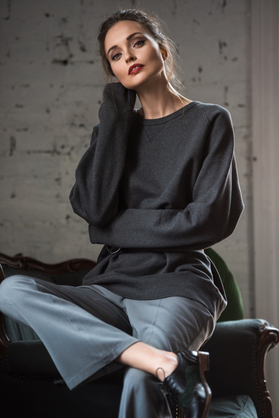 beautiful tender girl in grey jumper and pants sitting on armchair and looking at camera - Foto, Imagem