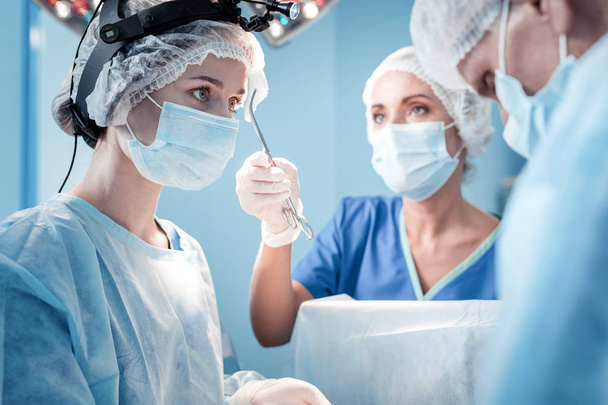 Nice serious surgeon looking at her colleagues - 写真・画像