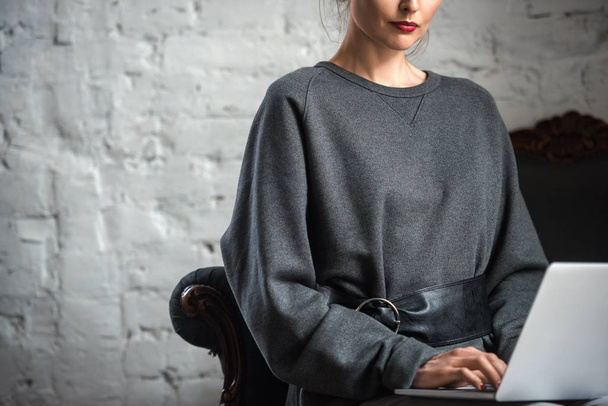 cropped shot of woman in grey stylish sweater using laptop indoors - Fotó, kép