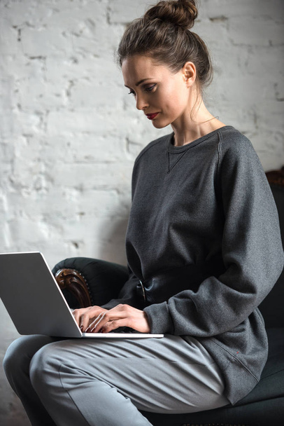 beautiful concentrated woman in grey clothes using laptop - Photo, Image