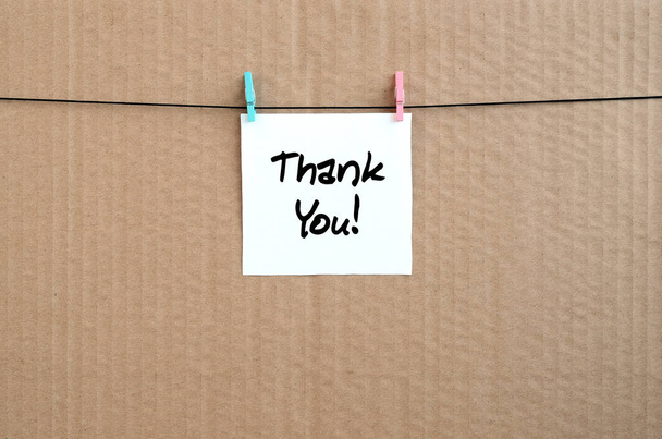 Dank u! Nota is geschreven op een witte sticker die hangt met een wasknijper op een touw op een achtergrond van bruin karton - Foto, afbeelding