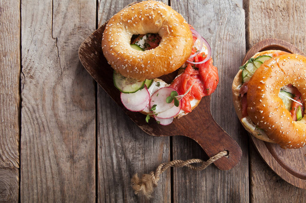 bagels with salmon fish and cream cheese with cucumber and fresh radish slices on wooden cutting boards, close-up  - Zdjęcie, obraz