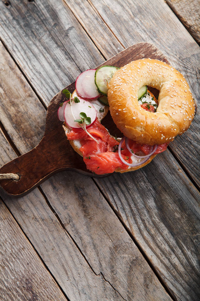 bagel with salmon fish and cream cheese with cucumber and fresh radish slices  on wooden cutting board , close-up  - 写真・画像