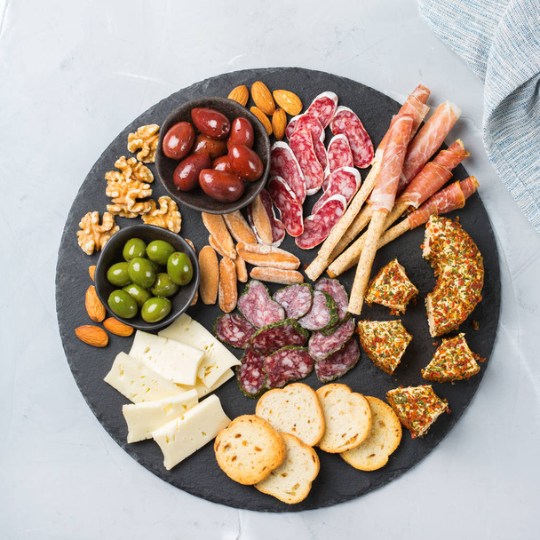 Still life, food and drink, holidays concept. Assortment of spanish tapas or italian antipasti with meat, ham, olives, cheese, nuts and bread on a table. Top view flat lay background - Photo, Image