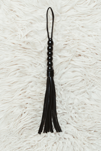 Black strict leather flogging whip on white carpet - Photo, Image