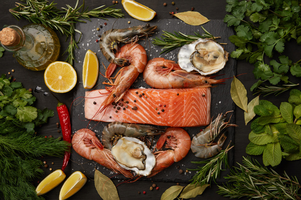 Raw salmon and assorted seafood with herbs and lemons on dark background - Photo, Image