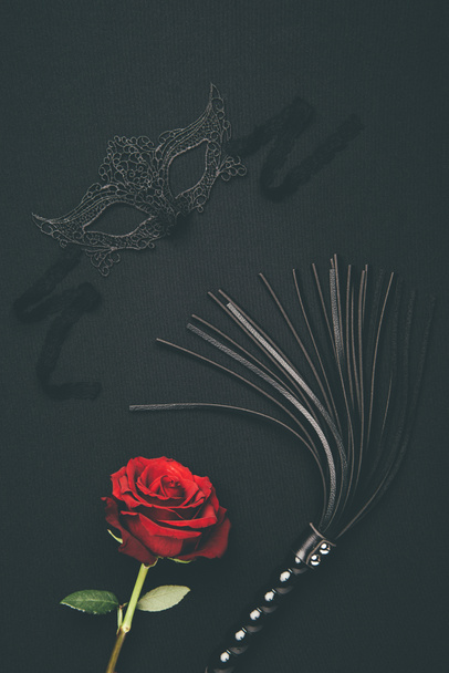 Máscara de encaje y látigo negro con flor de rosa aislado en negro
 - Foto, Imagen
