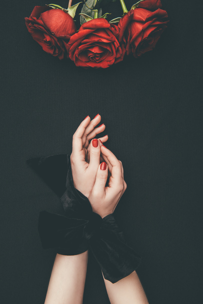 Female hands tied with ribbon and rose flowers isolated on black - Foto, Imagem