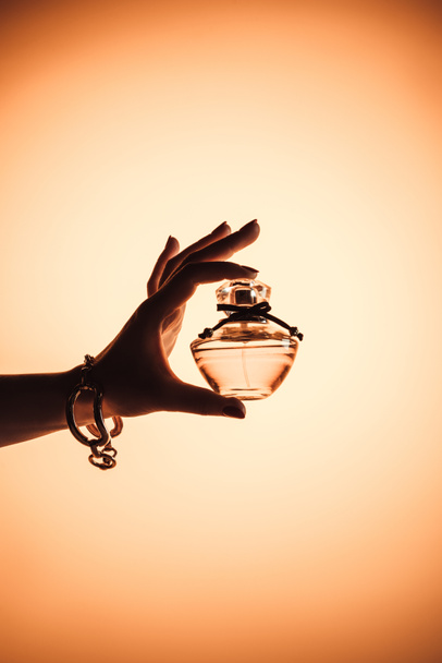 bijgesneden beeld van vrouwelijke hand met sensueel parfum in doorzichtige fles, geïsoleerd op geel - Foto, afbeelding