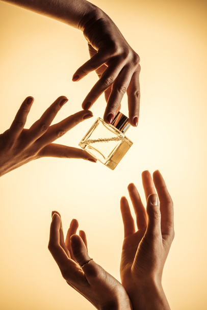 vista cortada de mulheres segurando garrafa de luxo de perfume, isolado em amarelo
 - Foto, Imagem
