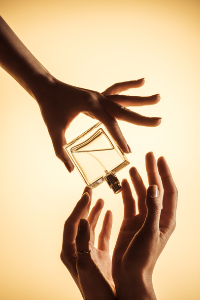 vista cortada de mulheres segurando garrafa de perfume de luxo, isolado em amarelo
 - Foto, Imagem