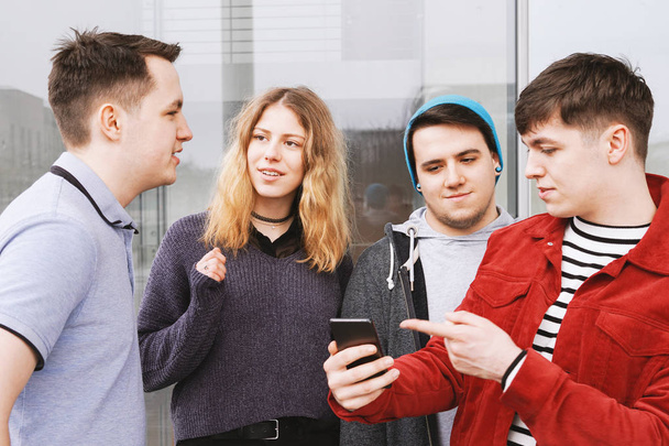grupo de amigos adolescentes teniendo una conversación mientras el joven está mostrando algo en su teléfono inteligente
 - Foto, Imagen