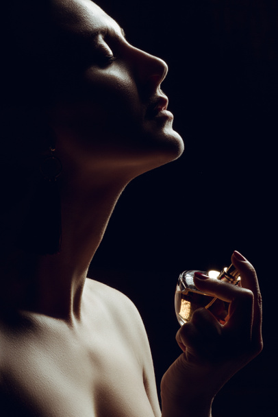 sylwetka Zmysłowa dziewczyna rozpylania perfum na szyi, na czarnym tle - Zdjęcie, obraz