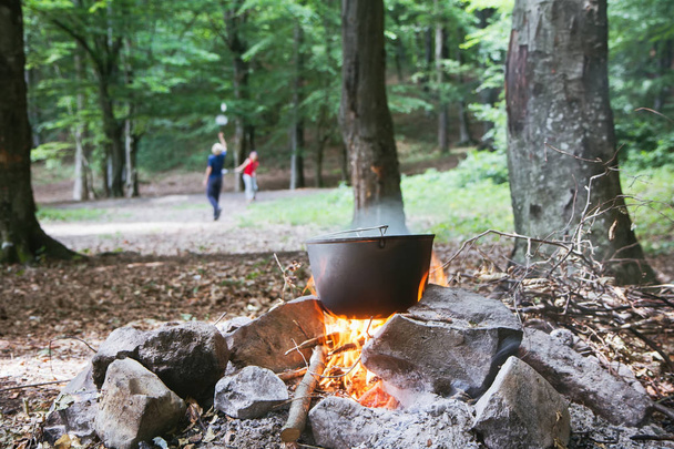 A cauldron with food at the fire and children playing badminton - Photo, Image