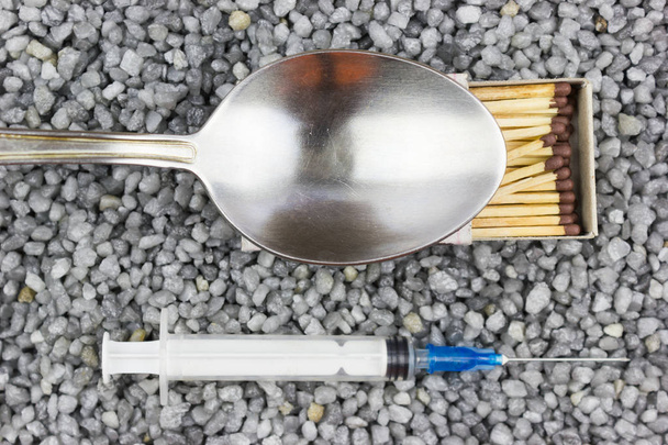 Plastic syringe, a spoon and a match on the fine gravel. Medicine, medicine. Taking drugs. - Zdjęcie, obraz